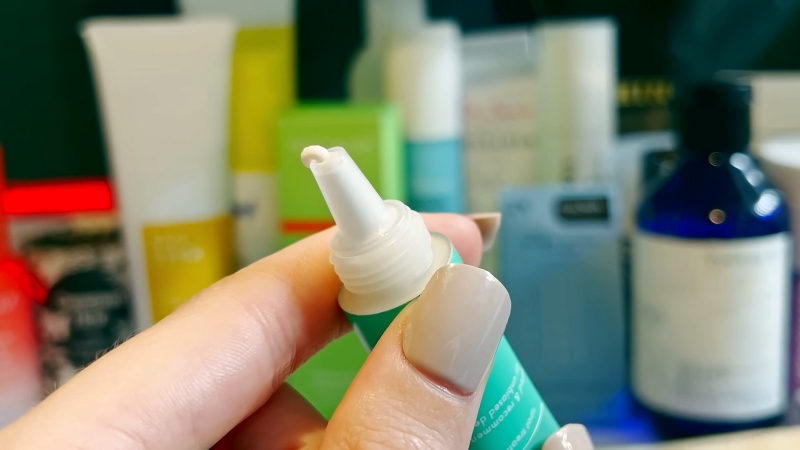 Hand holding a topical skincare tube with other treatment bottles in the background